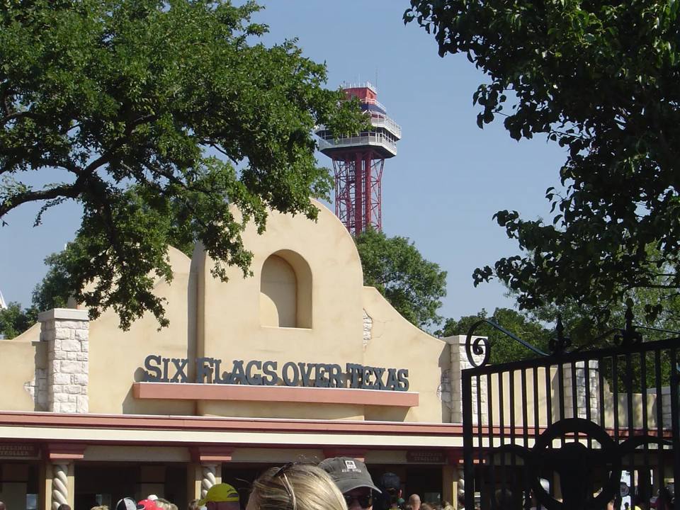 The Six Flags Over Texas entrance framed by trees, with Oil Derrick rising behind it.
