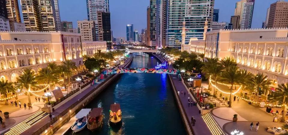 O canal de Al Qasba ao crepúsculo entre fachadas iluminadas.