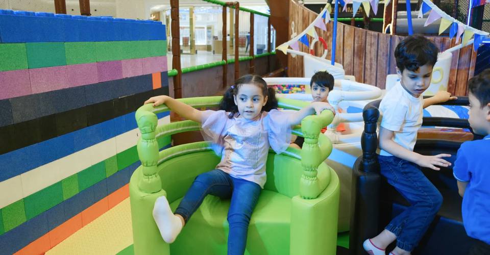 Children seated on a green ride in the colorful play area at 360 Play Bahrain.