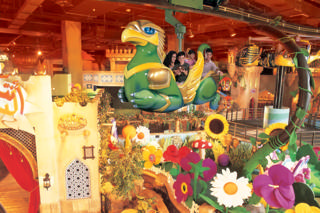 A large fantasy vehicle glides above giant flowers and oriental façades inside the park.