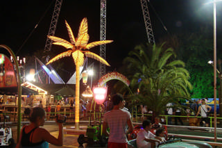 Antibes Land — A zona familiar à noite em redor de uma palmeira luminosa, com atrações e visitantes.