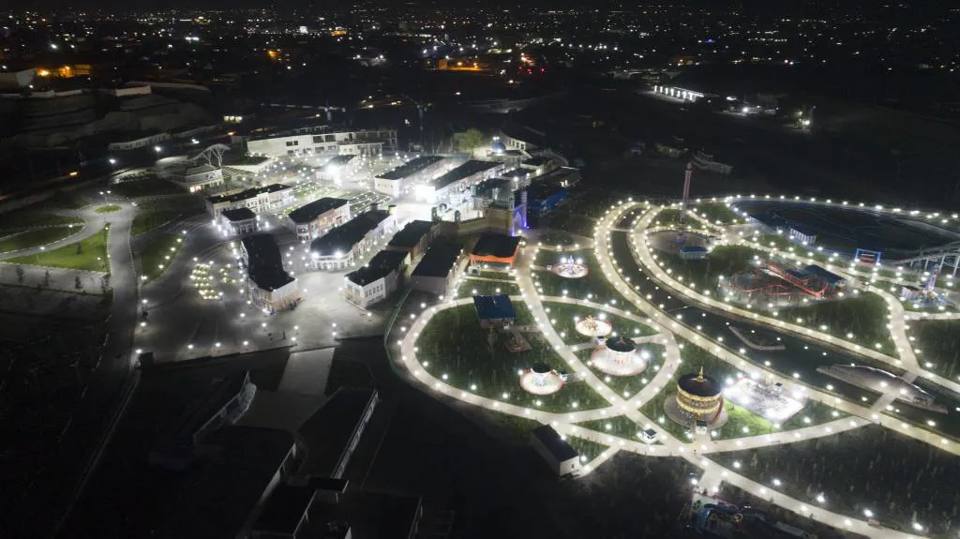 Vista aérea nocturna de Afsona Land con caminos y atracciones iluminados.
