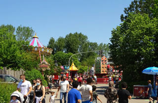 Tree-lined Kermisplein avenue bordered by rides and fairground scenery.