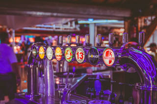 Fila de torneiras de bebidas sob luzes roxas num bar do Luna Park