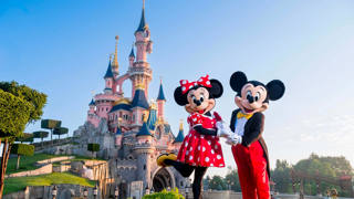 Mickey and Minnie stand before the pink Sleeping Beauty Castle in Disneyland Park.