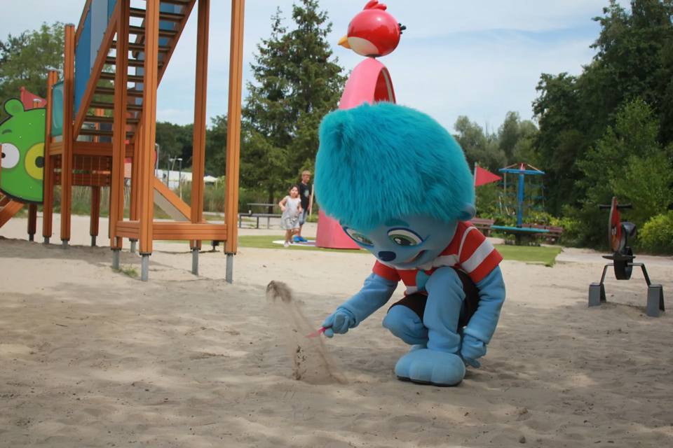 Mascot Dippie welcomes children around a large sandy play area.
