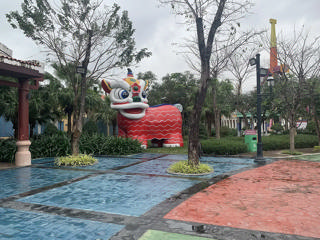 Um caminho colorido do Asia Park entre árvores, diante de um grande leão decorativo vermelho.