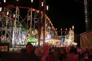 Antibes Land — A multidão na alameda principal iluminada, dominada por uma montanha-russa.