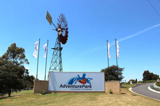 Placa de entrada do Adventure Park Geelong sob o moinho metálico e as bandeiras do parque.